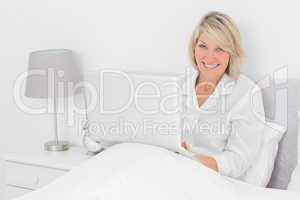 Happy woman sitting in bed with laptop looking at camera