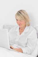 Content woman sitting in bed with laptop