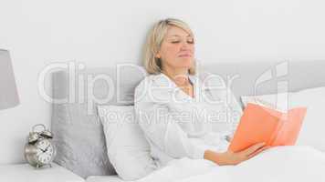 Blonde woman sitting in bed reading