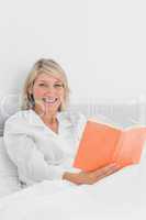Smiling woman sitting in bed reading