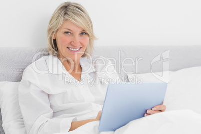 Blonde woman sitting in bed using tablet pc
