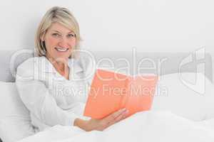 Blonde woman sitting in bed reading smiling at camera