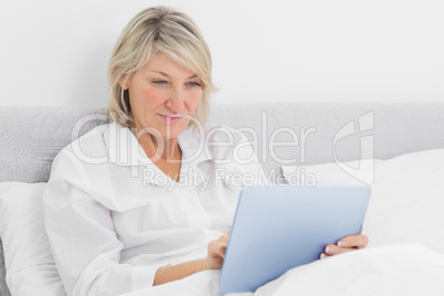 Happy woman sitting in bed using tablet pc