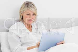 Happy woman sitting in bed using tablet pc