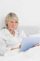 Cheerful woman sitting in bed using tablet pc