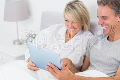 Laughing couple using tablet pc in bed