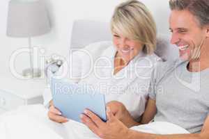 Laughing couple using tablet pc in bed