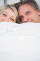 Couple smiling at camera from under the covers