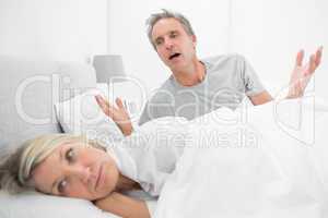 Man pleading with his upset partner in bed