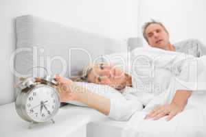 Woman in bed with partner turning off alarm clock