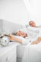 Blonde woman in bed with partner turning off alarm clock