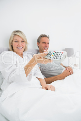 Cheerful couple watching tv in bed