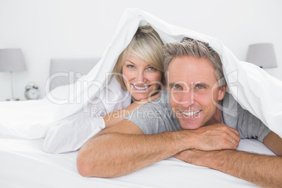 Happy couple smiling under the covers at the camera