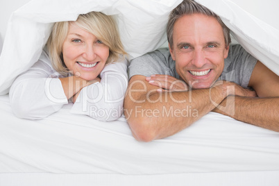Cheerful couple smiling under the covers at the camera