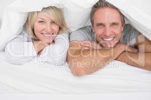 Cheerful couple smiling under the covers at the camera