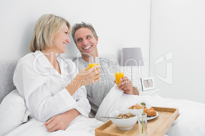 Cheerful couple having orange juice at breakfast in bed