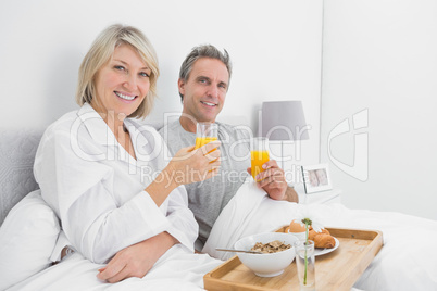 Happy couple having orange juice at breakfast in bed