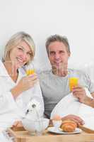 Content couple having orange juice at breakfast in bed