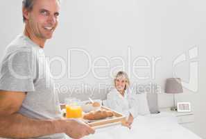 Cheerful man bringing breakfast in bed to his partner