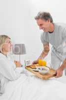 Smiling man giving breakfast in bed to his partner