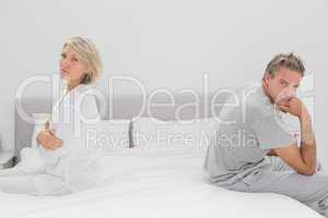 Couple sitting on opposite sides of bed looking at camera