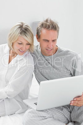 Couple using laptop sitting on bed