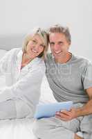 Couple using their tablet pc smiling at camera