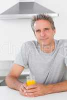 Happy man having glass of orange juice in kitchen