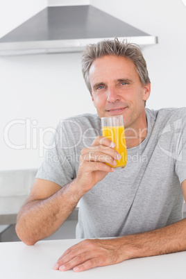 Cheerful man having glass of orange juice in kitchen