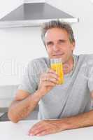 Cheerful man having glass of orange juice in kitchen