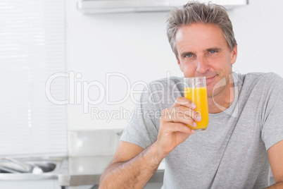 Smiling man having glass of orange juice in kitchen