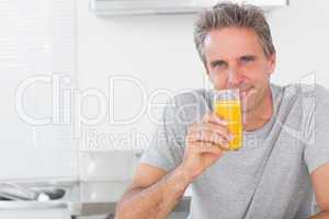 Smiling man having glass of orange juice in kitchen