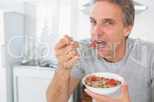 Happy man eating cereal for breakfast in kitchen