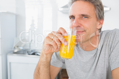 Happy man drinking orange juice in kitchen