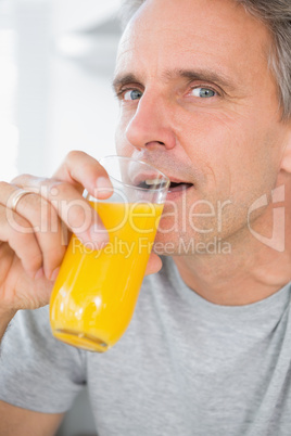 Cheerful man drinking orange juice in kitchen