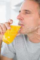 Content man drinking orange juice in kitchen