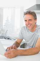 Smiling man using laptop in kitchen