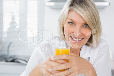 Happy blonde having orange juice in kitchen