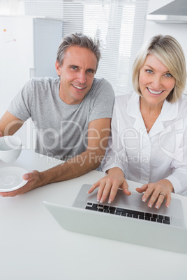 Cheerful couple using laptop in the morning looking at camera