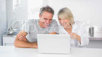 Happy couple laughing at laptop in the morning