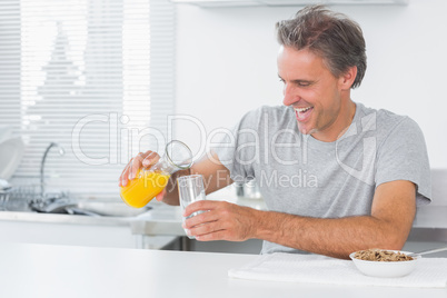 Happy man pouring orange juice for breakfast