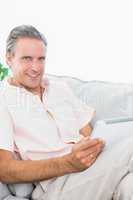 Happy man relaxing on his couch using tablet pc looking at camer