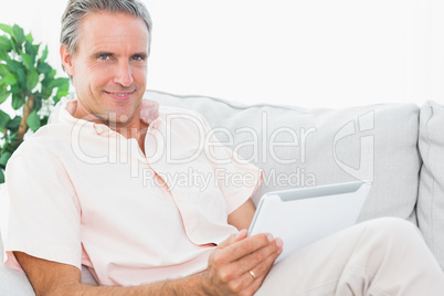 Cheerful man on his couch using tablet pc looking at camera