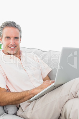 Smiling man on his couch using laptop looking at camera Smiling man on his couch using laptop looking at camera