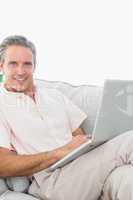 Smiling man on his couch using laptop looking at camera