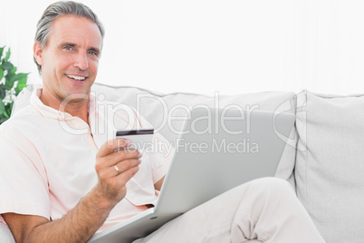 Happy man on his couch using laptop for shopping online