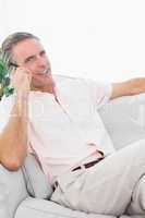 Man on his couch making phone call smiling at camera