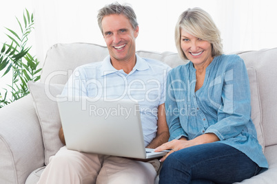 Happy couple using laptop together on the couch looking at camer