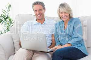 Happy couple using laptop together on the couch looking at camer