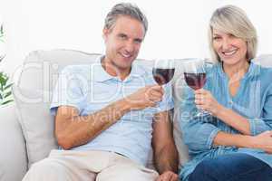 Couple toasting with red wine on the sofa looking at camera
